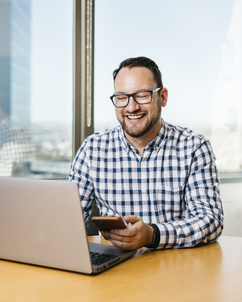 Tim McTigue wearing blue checkered shirt. Sitting at a computer, working. Set in an office